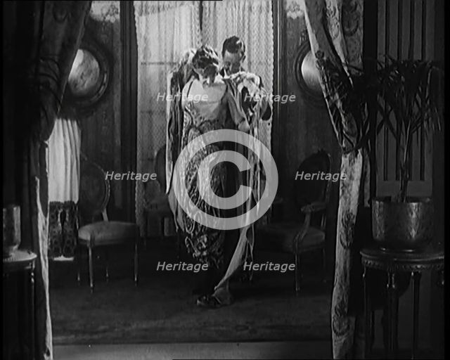 A Male Civilian Helping a Female Civilian Remove Her Fur Coat Revealing an Ornated Gown, 1920. Creator: British Pathe Ltd.