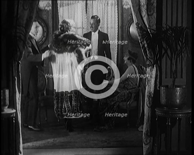 A Male Civilian Helping a Female Civilian Remove Her Fur Trimmed Coat Revealing an Ornated Gown, 192 Creator: British Pathe Ltd.
