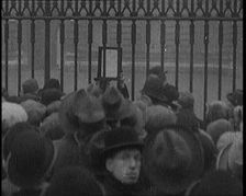A Male Civilian Holding up a Bulletin from the Doctor to Crowds Gathering Outside..., 1929. Creator: British Pathe Ltd