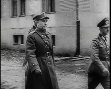 A Male Polish Army Commander Walking Past the Corner of a Large Building With Two Male... 1939. Creator: British Pathe Ltd