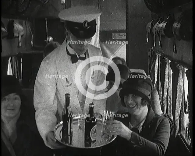 A Male Waiter Serves Smiling and Laughing Passengers Drinks  Inside an Aircraft, 1920s. Creator: British Pathe Ltd.