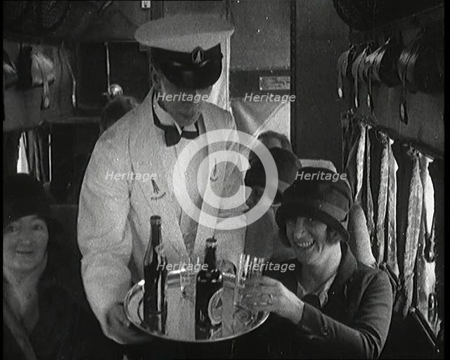A Male Waiter Serves Smiling and Laughing Passengers Drinks  Inside an Aircraft, 1920s. Creator: British Pathe Ltd.