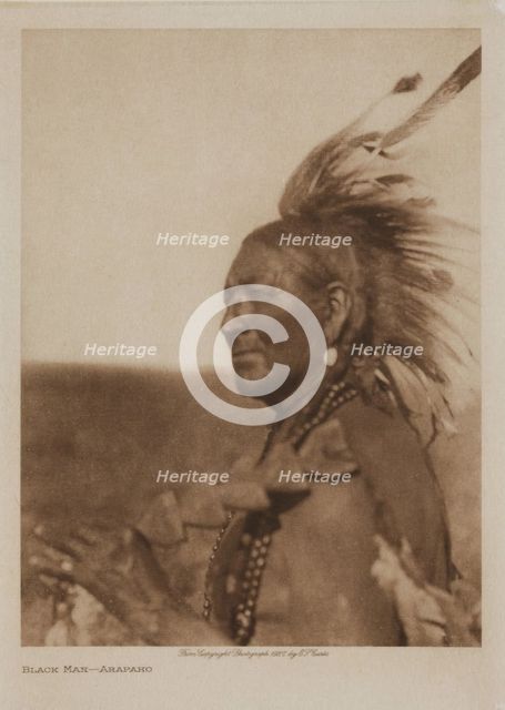 A Native American man from the Arapaho tribe wearing a feathered headdress, 1927. Creator: Edward Sheriff Curtis.