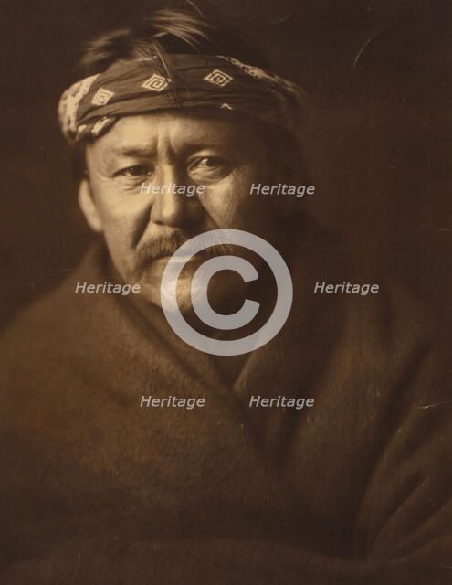 A Navajo man, head-and-shoulders portrait, wearing blanket and headband, facing front, c1904. Creator: Edward Sheriff Curtis.