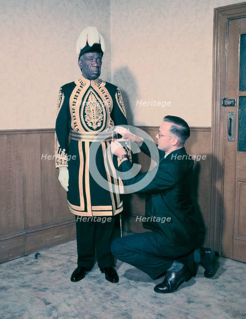 A Paramount Chief being fitted for his robes for the coronation of Queen Elizabeth II, 1953. Creator: Arthur Charles Kirby Ware.