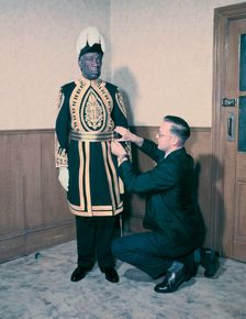 A Paramount Chief being fitted for his robes for the coronation of Queen Elizabeth II, 1953. Creator: Arthur Charles Kirby Ware