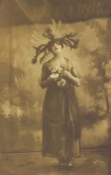 A performer in drag poses on stage wearing a head garment with sprawling feathers, [1910-1919?]. Creator: Unknown