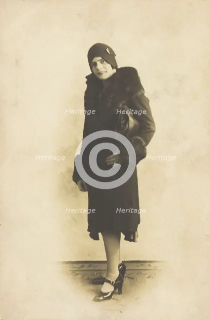 A person poses wearing a long coat with fur trim and a hat with a brooch, [between 1920 and 1929?]. Creator: Unknown.
