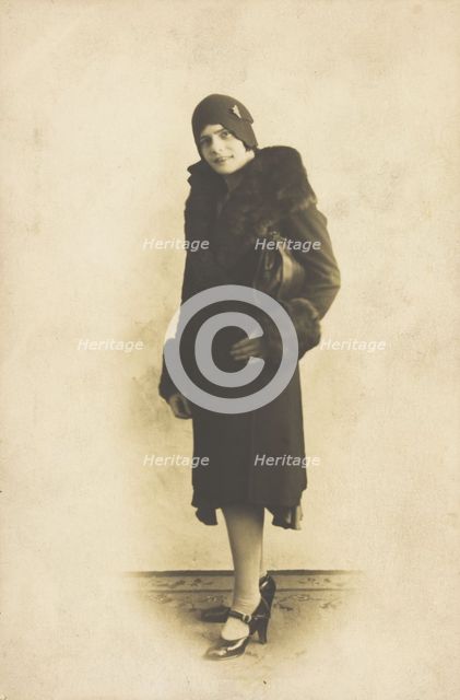 A person poses wearing a long coat with fur trim and a hat with a brooch, [between 1920 and 1929?]. Creator: Unknown.