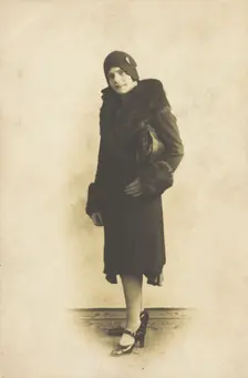A person poses wearing a long coat with fur trim and a hat with a brooch, [between 1920 and 1929?]. Creator: Unknown