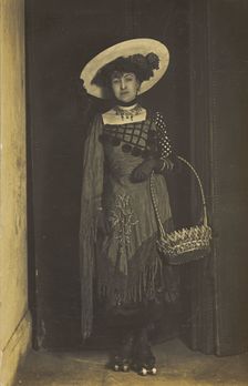 A person wearing a dress, large hat and roller skates, poses holding a basket, (1910-1919?). Creator: Unknown