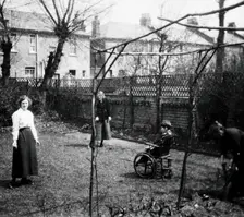 A physically disabled boy sitting in a wheelchair in the back garden of a semi..., c1910/1925. Creator: Unknown