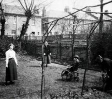 A physically disabled boy sitting in a wheelchair in the back garden of a semi..., c1910/1925. Creator: Unknown