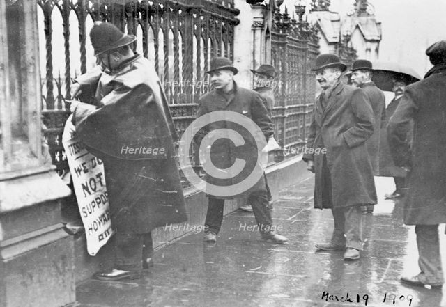 A policeman removes a suffragette poster from the railings, House of Commons, London, March 1909. Creator: Unknown.