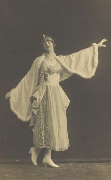 A prisoner of war in drag, wearing a dress and white cloak, poses...(between 1910 and 1919?). Creator: Albert Melzer