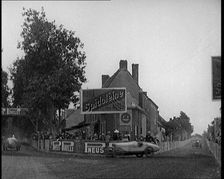 A Racing Circuit As Racing Cars Drive By. Signs On a Building Read: Spidoleine Huile and..., 1924. Creator: British Pathe Ltd