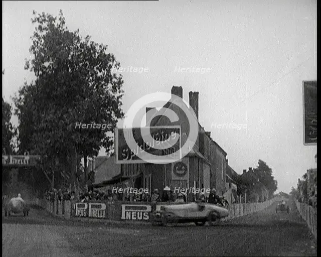 A Racing Circuit As Racing Cars Drive By. Signs On a Building Read: 'Spidoleine Huile' and..., 1924. Creator: British Pathe Ltd.