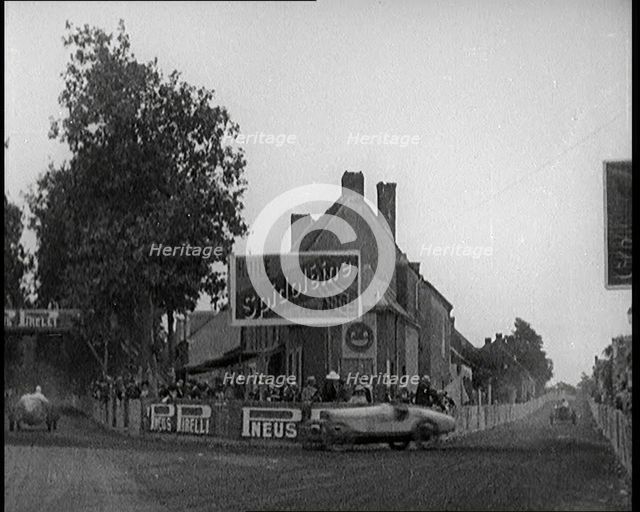 A Racing Circuit As Racing Cars Drive By. Signs On a Building Read: 'Spidoleine Huile' and..., 1924. Creator: British Pathe Ltd.