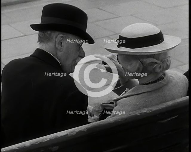 A Rear View of a Elderly Man and Woman Sitting on a Bench and Talking, Both Wearing Hats..., 1938. Creator: British Pathe Ltd.