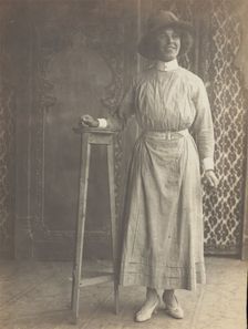 A sailor in drag leans on a high stool, in front of patterned scenery, (between 1910 and 1919?). Creator: Unknown