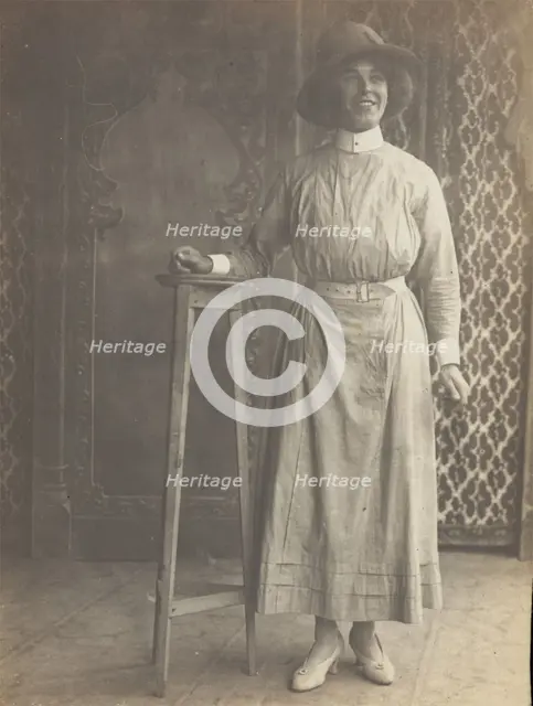A sailor in drag leans on a high stool, in front of patterned scenery, (between 1910 and 1919?). Creator: Unknown.