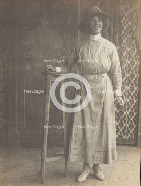 A sailor in drag leans on a high stool, in front of patterned scenery, (between 1910 and 1919?). Creator: Unknown.