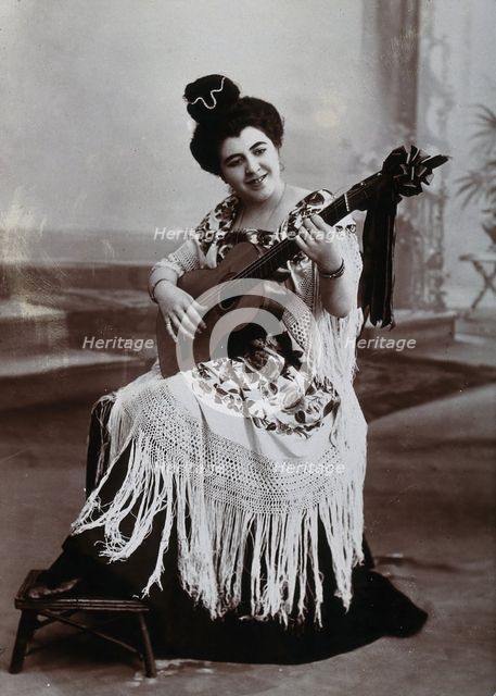 A seated woman, playing a guitar, wearing a fringed shawl, c1900. Creator: Unknown.