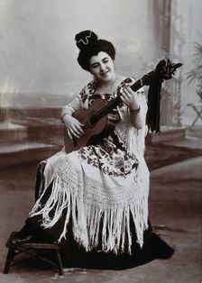 A seated woman, playing a guitar, wearing a fringed shawl, c1900. Creator: Unknown