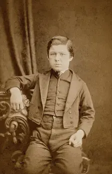 A seated young man with clenched fists, leaning against an ornate table, c1890s. Creator: AE Scales