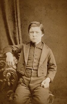 A seated young man with clenched fists, leaning against an ornate table, c1890s. Creator: AE Scales