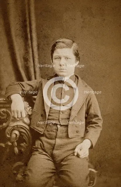 A seated young man with clenched fists, leaning against an ornate table, c1890s. Creator: AE Scales.