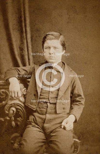 A seated young man with clenched fists, leaning against an ornate table, c1890s. Creator: AE Scales.