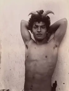 A Sicilian boy naked from the waist up, his hands behind his head, wearing horns, 3 Feb 1899. Creator: Count Wilhelm von Gloeden