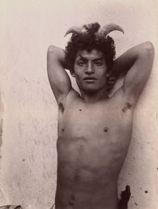 A Sicilian boy naked from the waist up, his hands behind his head, wearing horns, 3 Feb 1899. Creator: Count Wilhelm von Gloeden
