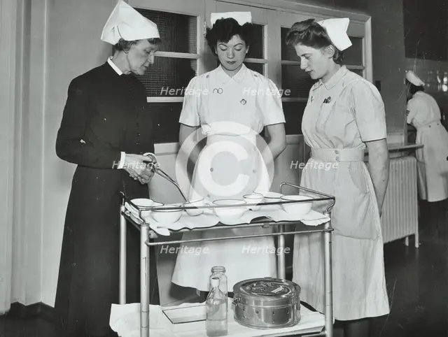 A Sister imparts knowledge and technical expertise to two trainee nurses, c1950s. Creator: Unknown.
