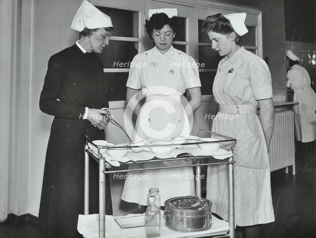 A Sister imparts knowledge and technical expertise to two trainee nurses, c1950s. Creator: Unknown.