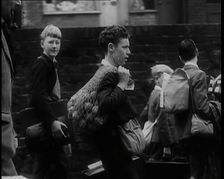 A Small Group of British Male Evacuees Carrying Bags and Walking Next to a Brick Wall, 1939. Creator: British Pathe Ltd