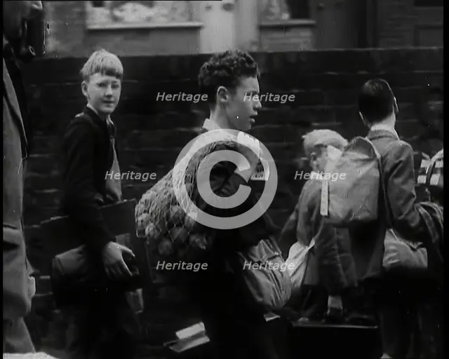 A Small Group of British Male Evacuees Carrying Bags and Walking Next to a Brick Wall, 1939. Creator: British Pathe Ltd.