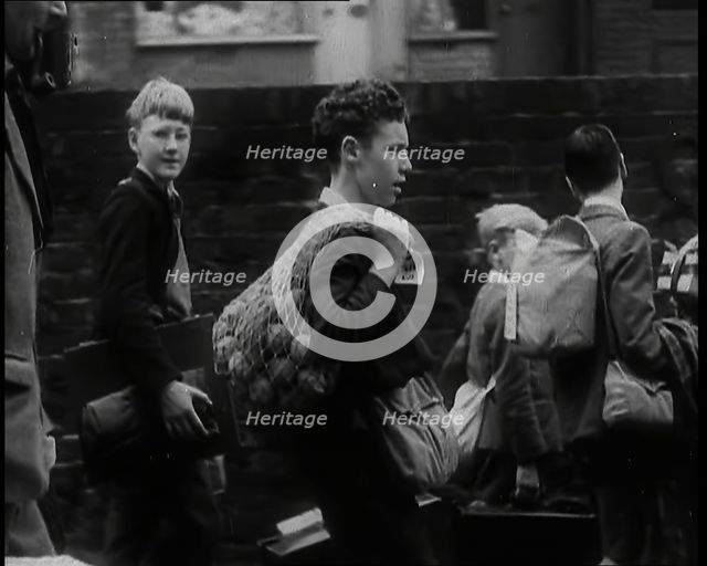 A Small Group of British Male Evacuees Carrying Bags and Walking Next to a Brick Wall, 1939. Creator: British Pathe Ltd.