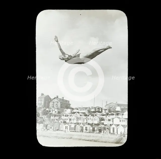 A swimmer diving into the sea at Southcliff, Walton-on-the-Naze, with beach huts on South..., 1920s. Creator: Norman Kingsley Harrison.