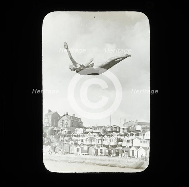 A swimmer diving into the sea at Southcliff, Walton-on-the-Naze, with beach huts on South..., 1920s. Creator: Norman Kingsley Harrison.