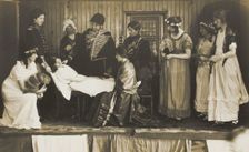 Amateur actors, some in drag, on stage attending to the death of a female character, [1910-1919?]. Creator: Unknown