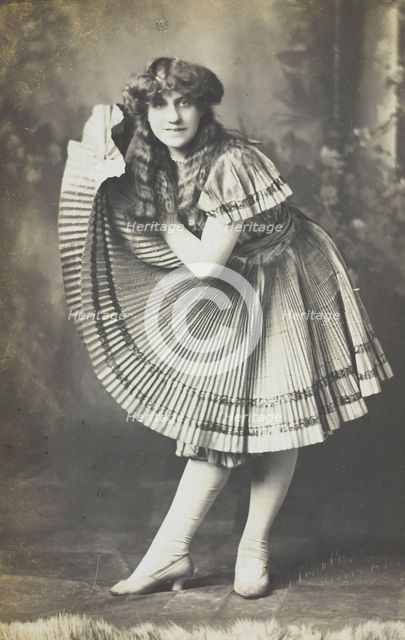 An amateur actor in drag holds up his impressive folded dress to one side, (between 1910 and 1919?). Creator: Unknown.