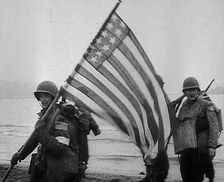 An American Soldier Holding an American Flag on a North African Beach as Part of Operation...1942. Creator: British Pathe Ltd