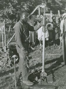 An African American man fixing a well's tube into the ground near Ridge, Maryland, July 1941. Creators: Farm Security Administration, John Collier