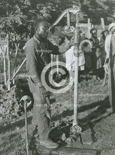 An African American man fixing a well's tube into the ground near Ridge, Maryland, July 1941. Creators: Farm Security Administration, John Collier.