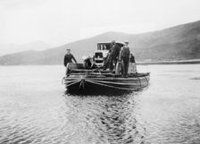 An early ferry transporting a car across a lake