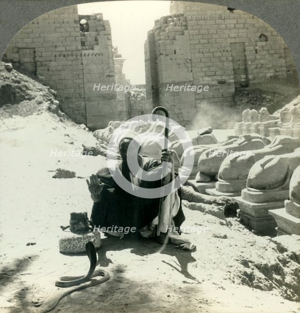 'An Egyptian Snake Charmer Piles His Trade Beside the Avenue of Sphinxes, Temple of Karnak, Thebes,  Creator: Unknown.