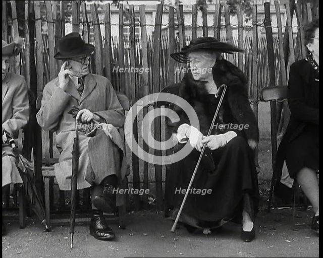 An Elderly Woman Wearing a Wide Hat, a Fur Stole, and Holding a Walking Stick Sitting on a..., 1938. Creator: British Pathe Ltd.