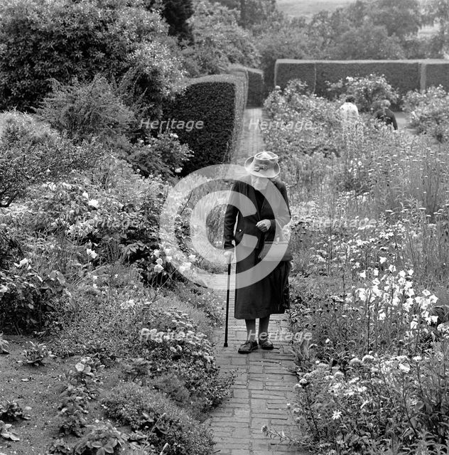 An elderly lady walking in a flower garden in Aldeburgh, Suffolk,1956. Artist: John Gay